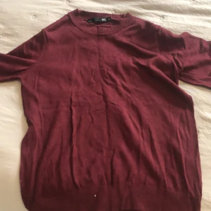 Vinröd stickad topp från 157 - En enkel vinröd stickad topp från 157 med rund halsringning och korta ärmar. Toppen har en klassisk, rak passform och är tillverkad i ett mjukt stickat material som passar perfekt till både jeans och kjol.