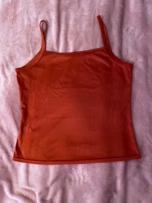 Rostbrun linnetopp med smala band - Enkel och stilren rostbrun linnetopp med tunna axelband. Toppen har en rak passform och ärmlös design, perfekt för varma dagar. Materialet känns mjukt och lätt mot huden.