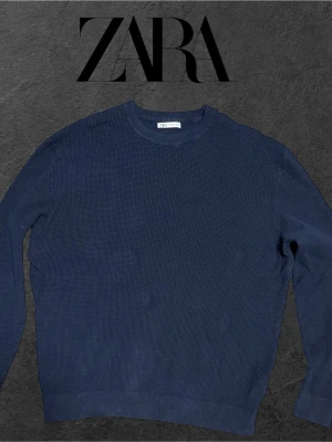 Mörkblå stickad tröja från Zara - En stilren mörkblå stickad tröja från Zara med rund halsringning och lång ärm. Tröjan har en diskret struktur i materialet och ribbade muddar vid ärmslut och nederkant. Perfekt för lager på lager under kyliga dagar.