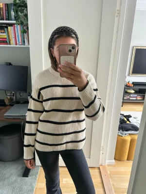 Randig stickad tröja i beige och svart - Säljer en beige stickad tröja med svarta horisontella ränder. Tröjan har en avslappnad passform, rund halsringning och långa ärmar. Perfekt för dig som gillar en enkel men snygg stil.
