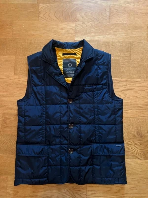 Mörkblå quiltad dunväst Oscar Jacobson - Quiltad mörkblå dunväst från Oscar Jacobson med gul insida. Köpt för 2999 och knappt använd och är i storlek M 