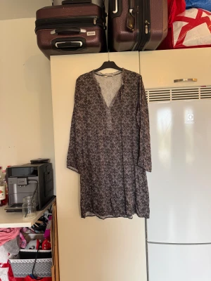 Mönstrad svart/grå kortklänning - Säljer en luftig kortklänning med svart och grått mönster, v-ringning och knappar framtill. Klänningen har långa ärmar och ett snyggt, detaljerat mönster över hela tyget. Perfekt för dig som gillar en avslappnad men ändå stilren look. Från märket Odd Molly. Storlek 3 som enligt deras storleksguide motsvarar en L. Mycket fint skick, jag hittar inga synliga anmärkningar eller defekter. 