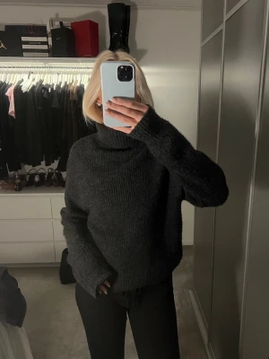 Mörkgrå stickad polotröja - Mysig mörkgrå stickad polotröja med oversized passform och långa ärmar. Tröjan har en hög polokrage och är perfekt för kalla dagar. Enkel och stilren design som passar till allt.