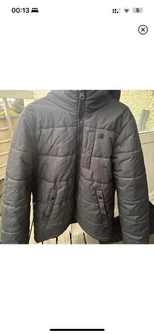 Svart pufferjacka från G-Star RAW L ( - Väl fodrad pufferjacka från G-Star RAW i storlek L. Jackan har quiltad design, huva, dragkedja framtill och praktiska fickor med knappar. Perfekt för kalla dagar och har en clean streetstil med diskret logga på bröstet. 