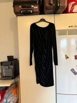 Svart sammetsklänning med rynk - Snygg svart sammetsklänning med långa ärmar och rynkade detaljer framtill. Klänningen har en kort längd och en klassisk rund halsringning. Perfekt för dig som gillar en elegant och stilren look med lite extra edge. Storlek M. Helt ny med tags/ prislapp fortfarande kvar. 