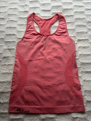 Persikrosa träningstopp från Power Energy - Säljer en sportig  linnetopp från Power Energy i storlek XS/S. Toppen har racerback och är tillverkad i ett snabbtorkande material med 41% polyester, 55% nylon och 4% elastan. Perfekt för gymmet eller löpning, med snygga meshdetaljer på sidorna.