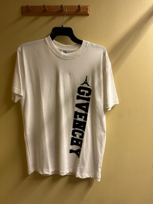 Vit Givenchy t-shirt med tryck - Vit t-shirt från Givenchy i mjuk bomull med svart vertikalt logotyptryck och Eiffel-tornet på framsidan. Baksidan har en stilren svart Eiffel-torn-grafik vid nacken. Klassisk passform och rund halsringning.