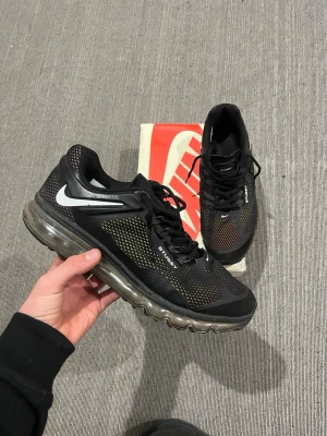 Nike Air Max x Stussy svarta sneakers - Nike Air Max x Stussy sneakers i svart med mesh-överdel och vita detaljer. Snygg design med synlig Air Max-sula, snörning och Stussy-logga på sidan. Skorna har rund tå och platt sula, och är tillverkade i syntetmaterial och mesh för en sportig vibe.