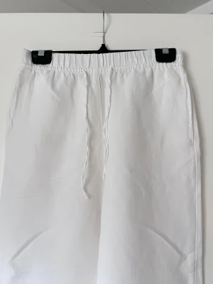 Vita linnebyxor från H&M - Säljer ett par fräscha vita linnebyxor med elastisk midja och snörning. Byxorna har rak och loose passform, vilket gör dem riktigt sköna och luftiga. Perfekta för varma dagar och chill stunder. Materialet är linne och färgen är helvit.