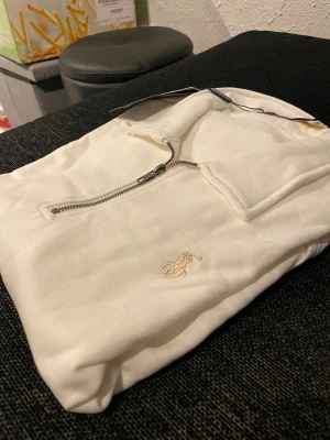 Polo Ralph Lauren zip hoodie  - Säljer en helt ny och oanvänd Polo Ralph Lauren half-zip tröja i vitt. Modellen har klassisk krage, broderad logga och dragkedja vid halsen. Aldrig använd – lappen sitter kvar.  Skick: Ny / oanvänd Färg: Vit Storlek: M Passform: Normal  Säljer då den inte kommit till användning. 