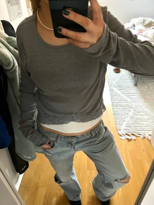 Grå långärmad tröja med spets från Hollister - Supersöt grå långärmad tröja från Hollister med rund hals, ribbad struktur och spetsdetalj längs nederkanten. Storlek L men väldigt liten i modellen (har vanligtvis xs/s)