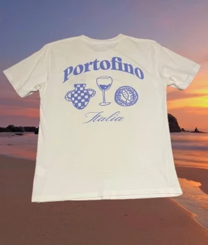 Vit Portofino graphic tee från Vailent - Vit t-shirt från Vailent med blått Portofino-tryck både fram och bak. Motiven inkluderar en vas, ett vinglas och en myntliknande symbol samt texten 'Italia'. Klassisk passform och rund hals, tillverkad i mjuk bomull. Passar mig som brukar ha storlek M men passar också såklart S