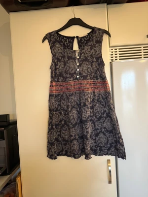Mörkblå ärmlös blus med spets - Supersöt mörkblå blus med vitt paisleymönster och broderade detaljer i rött och rosa över midjan. Ärmlös modell med knappar framtill och snygg spets i nacken. Perfekt för dig som gillar boho-vibe och lätta material. Storlek 1 som enligt deras storleksguide motsvarar en S. kanske kan vara något rymlig i storlek. Mer använd men fortfarande fint skick. 