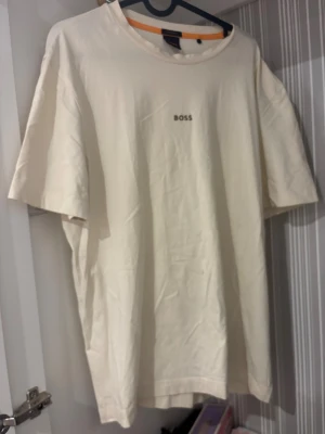 Vit relaxed fit t-shirt från BOSS - Säljer en stilren vit t-shirt från BOSS med relaxed fit. T-shirten har korta ärmar, rund halsringning och diskret BOSS-logga broderad på bröstet. Tillverkad i mjuk bomull för en skön känsla och avslappnad look.