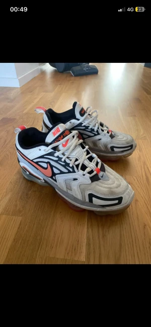 Nike Vapormax sneakers vit/svart/röd - Nike Vapormax sneakers i vitt, svart och rött med coola detaljer och synlig luftbubbla i sulan. Snygg design med mesh och syntetpaneler, snörning och röd swoosh på sidan. Perfekta för dig som gillar streetstyle och sportig vibe.