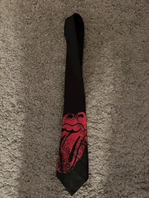 Svart slips med röd Rolling Stones-tryck - Helt ny slips med Rolling Stones. Bredd nertill 10 cm.