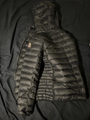 Svart dunjacka från Parajumpers L - Säljer en svart dunjacka från Parajumpers i storlek L men passar M väldigt bra också, Jackan är quiltad, har huva och dragkedja framtill. Lättviktig modell med klassisk Parajumpers-logga på ärmen och snygga detaljer. Perfekt för kalla dagar när du vill hålla stilen. Den har inga skador eller liknande 