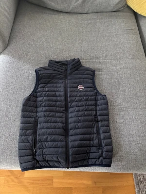 Mörkblå dunväst från Colmar, 16Y - Snygg svart dunväst från Colmar med quiltad design och dragkedja framtill. Västen har två fickor med dragkedja och en liten logga på bröstet. Perfekt för lager-på-lager och enkel att matcha med olika outfits.