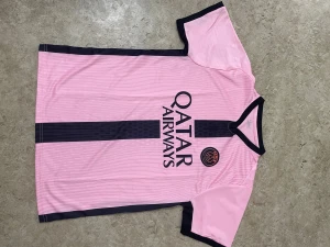 Fotbollströja  - Bilderna visar en rosa och svart fotbollströja från Paris Saint-Germain med Qatar Airways-logga, inte skor.