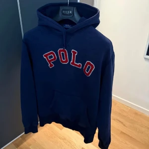  Polo Ralph Lauren Tröja  - Mörkblå POLO-hoodie i fint skick. Klassisk modell med röd/vit logotyp, huva med dragsnören och känguruficka. Mjuk, bekväm och perfekt för vardagsbruk.