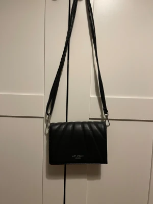 Svart quiltad axelväska Art Street - Snygg svart axelväska från Art Street London i quiltad design. Väskan har ett stilrent utseende med avtagbar axelrem och flera fack inuti. Tillverkad i skinnimitation och passar perfekt när du vill ha med det viktigaste.