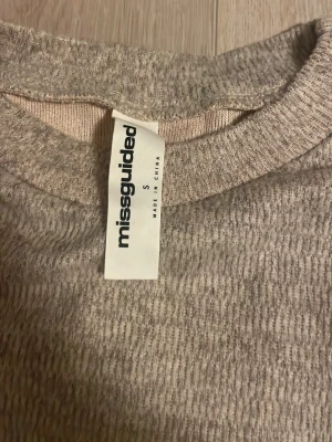 Beige stickad topp från Missguided - Säljer en beige stickad topp från Missguided i storlek S. Modellen har bred midja och korta, nästan ärmlösa axlar med avslappnad passform. Materialet är mjukt och ribbat, perfekt för dig som gillar chill och enkel stil.