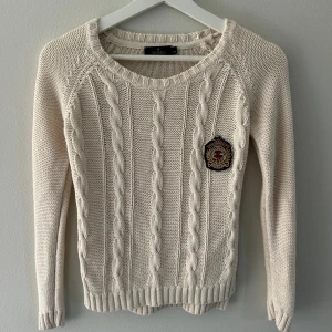 Beige kabelstickad tröja från Morris - Kabelstickad beige tröja från Morris med rund halsringning och ett broderat emblem på bröstet. Bra skick och storlek xs.