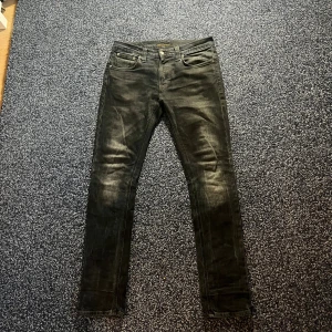 Nudie Jeans   - Modellen är Tape Ted. Dom är svart/blåa. storlek 31/32. Jeansen har klassisk femficksdesign, svarta sömmar och diskret Nudie-logga på bakfickan. Snyggt slitna detaljer och smal passform som sitter tajt hela vägen ner.
