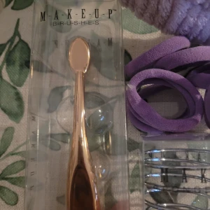 Makeupborste och beautyblender-hållare - Säljer en oval makeupborste i roséguld med ergonomiskt handtag, perfekt för foundation eller contour. Medföljer en spiralformad beautyblender-hållare i silvermetall som håller din svamp fräsch. Flera lila scrunchies och ett fluffigt lila hårband med rosett ingår. O snoddar lila