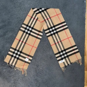 Burberry Halsduk  - Klassisk beige halsduk från Burberry i 100% kashmir med ikoniskt rutigt mönster. Använd ett tiotal gånger, i perfekt skick. Inköptes förra året men kom inte särkilt mycket till användning.   Inget kvitto finns då jag som sagt haft den i ca ett år nu därav såklart svårt att bevisa äkthet. Men den är köpt på the local store i Skellefteå så den är 100% äkta och om ni vill vara säker så rekommenderar jag att ni gör en egen äkthets check 👍