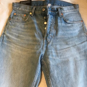 Weekday ljusblå raka jeans - Snygga ljusblå jeans från Weekday med klassisk femficksdesign och raka ben. Hög midja och knappgylf ger en retrovibe. Jeansen är tillverkade i bomull och har en clean, enkel look som funkar till allt. Perfekt för dig som gillar stilrena och tidlösa jeans. Helt oanvända. Prislapp kvar. Stl 27/30