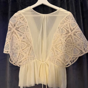 Vit blus från Zara - Supersöt vit blus från Zara med broderade spetsärmar och knyt i ryggen. Klänningen har en luftig, kort modell med v-ringning och transparenta detaljer. Perfekt för dig som vill ha en snygg outfit(Oanvänd endast testad)🥰