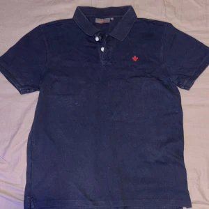 Mörkblå Morris Piké - En stilren och klassisk Morris piké i mörkblå färg med ett rött broderat märke 