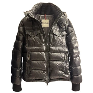 Svart Moncler dunjacka med huva - Äkta✅                                                             Säljer en svart dunjacka från Moncler med glansig finish, huva och dragkedja framtill. Jackan har två bröstfickor med lock och två sidofickor med dragkedja. Ribbstickad mudd vid kragen och klassisk pufferstil. Perfekt för kalla dagar. Övre dragkrok är borta men funkat utmärkt att lösa upp/ner👍🏻Köpt och verfierad på Vestiare collective, Kvitto finns