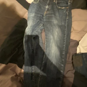 Blå jeans W32 L36 - Säljer ett par klassiska blå jeans med snygga slitningar och raka ben. Jeansen har fem fickor och normal passform, perfekta för dig som gillar en tidlös stil. Materialet är tåligt denim som håller länge. Kan gå ner i pris vid snabb affär 