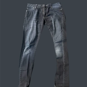 Svarta slim jeans från Acne Jeans - Säljer ett par svarta slim jeans från Acne Jeans med klassisk femficksdesign och läderpatch bak i midjan. Jeansen har smal passform, raka ben och är tillverkade i ett stretchigt bomullsmaterial för extra komfort.