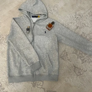 Grå hoodie från Polo Ralph Lauren - Använd fåtal gånger .                                   Size M men passar S !!!!!                              Snygg grå hoodie från Polo Ralph Lauren med klassisk blå logga på bröstet. Tröjan har huva, dragkedja och två fickor framtill. Tillverkad i mjuk bomull som är skön att ha på sig. Perfekt för chill dagar och enkel att matcha med jeans eller joggers.