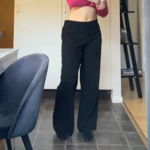 Svarta wide kostymbyxor med resår - Svarta kostymbyxor med breda ben och elastisk midja. Byxorna har en clean look utan fickor och stängs med dragkedja i sidan. Materialet är lite prassligt och har lite stretch