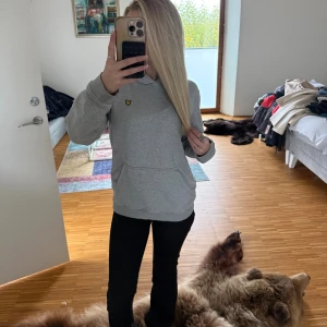 Grå hoodie från Lyle & Scott - Grå hoodie från Lyle & Scott med klassisk gul logga på bröstet. Tröjan har huva, känguruficka och är långärmad. Perfekt basic med relaxed vibe och mjukt material som passar till allt. passar xs/s