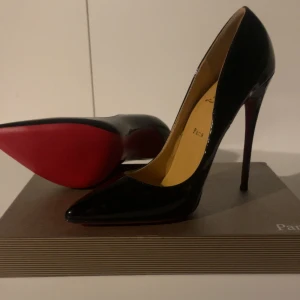 Christian Louboutin svarta pumps - Säljer ett par ikoniska svarta pumps från Christian Louboutin med klassisk röd sula. Skorna har spetsig tå, hög klack och är tillverkade i glansigt skinn. Perfekta för dig som vill sticka ut med en lyxig och tidlös look. Storlek 38