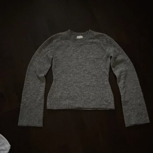 Grå stickad tröja från H&M XS - Snygg grå stickad tröja från H&M i storlek XS. Tröjan har rund hals, långa ärmar och breda ribbade muddar vid ärmslut och nederkant. Materialmixen består av polyester, akryl, ull och elastan vilket gör den både mjuk och bekväm. Perfekt för kyliga dagar.