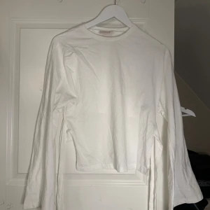 Vit långärmad tröja med knyt från Nelly - Säljer en vit långärmad tröja från Nelly i mjuk bomull. Tröjan har coola knytband i sidan som kan knytas i ryggen för en snygg detalj. Passar dig som gillar stilrena och enkla plagg med en twist. Tröjan har lite större armar och är lite större över bysten men sitter tajt kring midjan. 