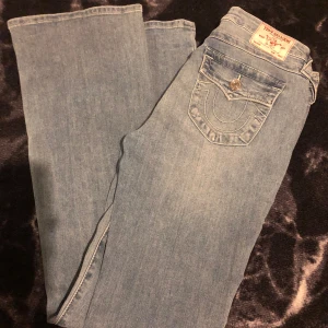 True Religion Becca Bootcut Jeans ljusblå - Helt nya, endast provade. Ljusblå jeans från True Religion, modell Becca Mid Rise Bootcut. Klassisk femficksdesign med snygga detaljer på bakfickorna och silverfärgade knappar. Jeansen har en bootcut-passform och är tillverkade i mjukt denimtyg. Storlek 29. Inköpta på Raglady för 1299kr, kvitto finns. Säljes pågrund av att de är för stora.