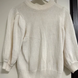 Vit stickad tröja från Gina Tricot - Säljer en krämvit stickad tröja från Gina Tricot i storlek M. Tröjan har rund halsringning, ribbade muddar och långärmade puffärmar som ger en trendig siluett. Perfekt för lager-på-lager under kyliga dagar.