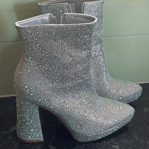 Glittriga silver boots med klack - Säljer ett par boots i silver med glittriga paljetter och stenar över hela skon. De har en hög klack och plattform, samt spetsig tå. Perfekt för dig som vill sticka ut med ett riktigt statement-plagg. Skorna har dragkedja på insidan för enkel påtagning. Storlek 40. Klacken är 12 cm. 😍✨🩶 Köpta för 400 men säljer för 350, använt dessa en gång! 