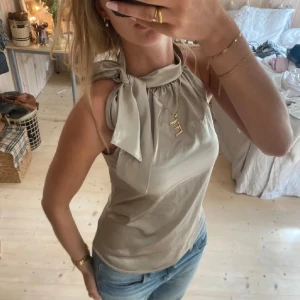 Beige linnetopp med knyt i halsen - Säljer en beige festtopp med snygg knytning i halsen. Toppen är ärmlös och har en liten krage. Köpte den här på plick. Säljer då den inte kom till användning🥰