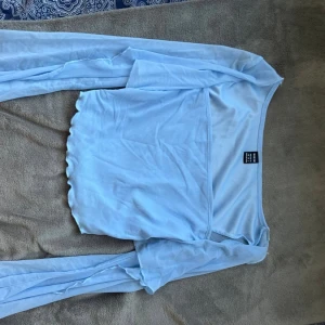 Ljusblå mesh offshoulder topp SHEIN - Säljer en ljusblå offshoulder topp från SHEIN i meshmaterial. Toppen är croppad med långa ärmar och har vågig kant nertill för en extra söt touch. Perfekt för dig som gillar trendiga och luftiga plagg.