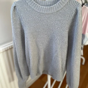 Grå stickad tröja från Monki - Säljer en grå stickad tröja från Monki i storlek S. Tröjan har en ribbad struktur, rund halsringning och långa ärmar med lätt puff vid axlarna.
