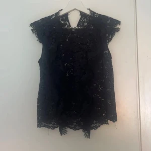 Mörkblå spetsblus från Zara - Säljer en mörkblå blus från Zara i vacker spets med blommigt mönster. Blusen är ärmlös med volangdetaljer vid axlarna och har en rund halsringning. Perfekt för dig som gillar romantiska och feminina plagg. 