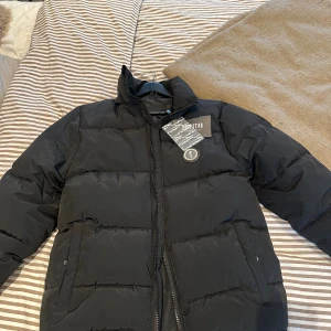 Svart pufferjacka från Trapstar - Säljer en svart pufferjacka från Thorstar i storlek M. Jackan har hög krage, dragkedja framtill och två stora fickor. Perfekt för kalla dagar och har en clean streetstyle-look. Jackan är vadderad och har en snygg badge på bröstet.